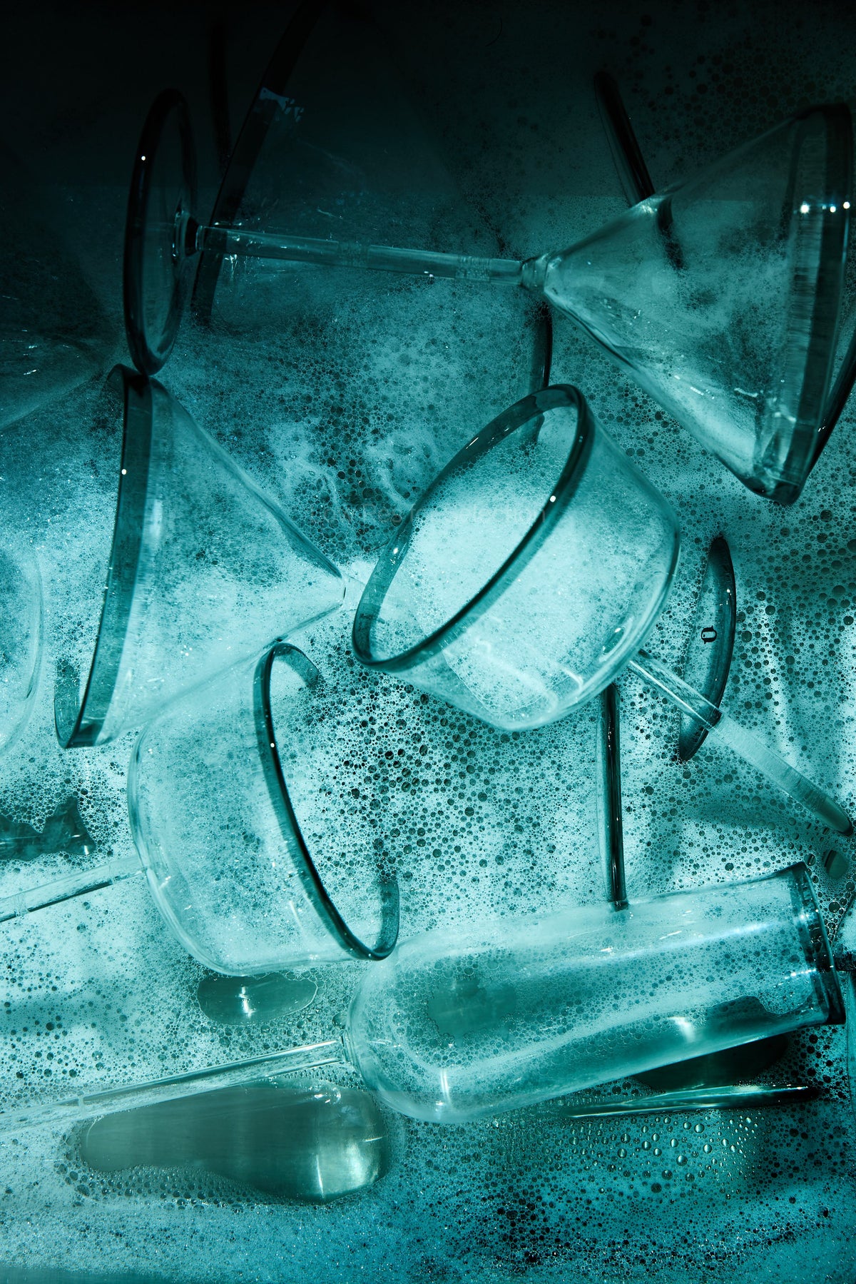 A cluster of drinking glasses with dark rims scattered on a textured, foamy surface under a strong blue-green tint.