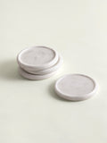 Four round white marble coasters, with three stacked and one standing upright, on a light cream background.
