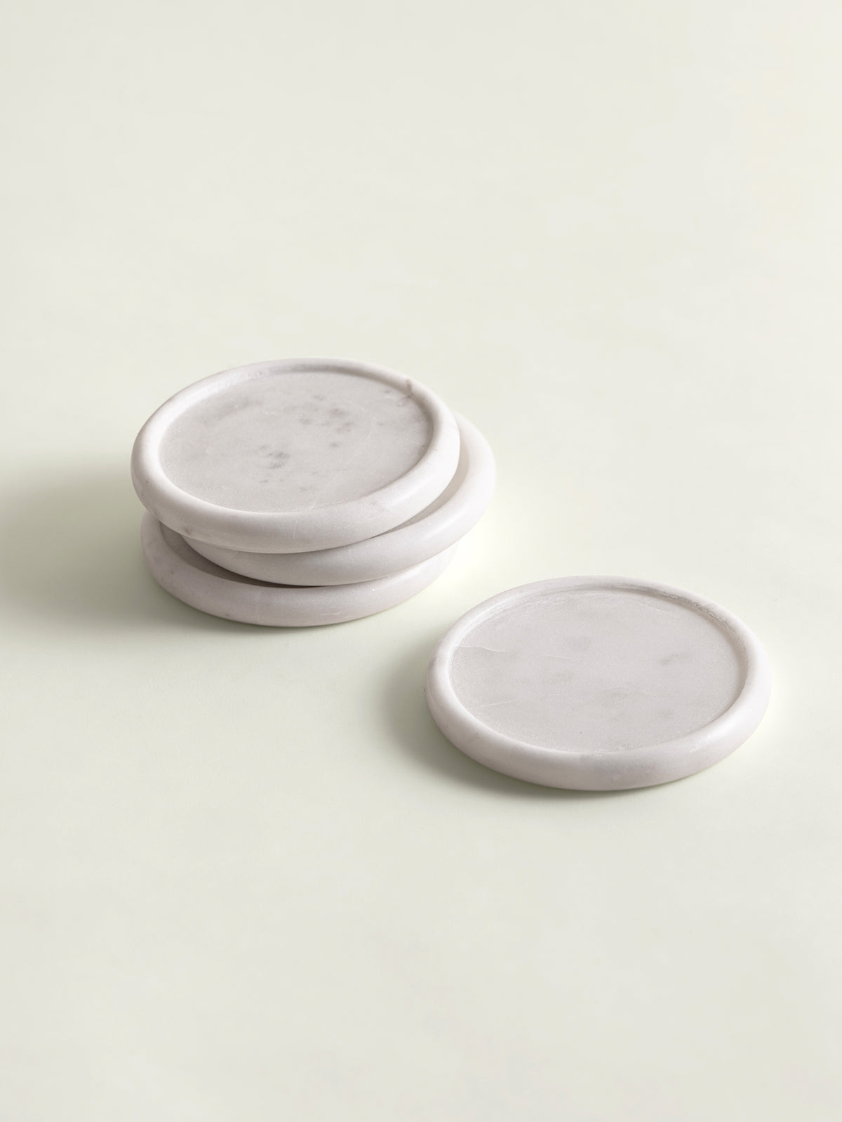 Four round white marble coasters, with three stacked and one standing upright, on a light cream background.