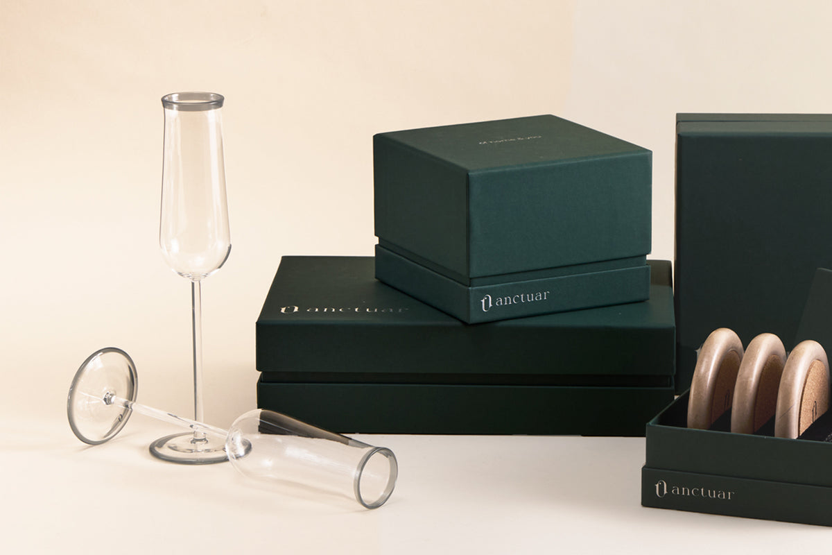 A set of lipp champagne flutes and gift packaging on a warm beige background, and a gift box with round wooden coasters.
