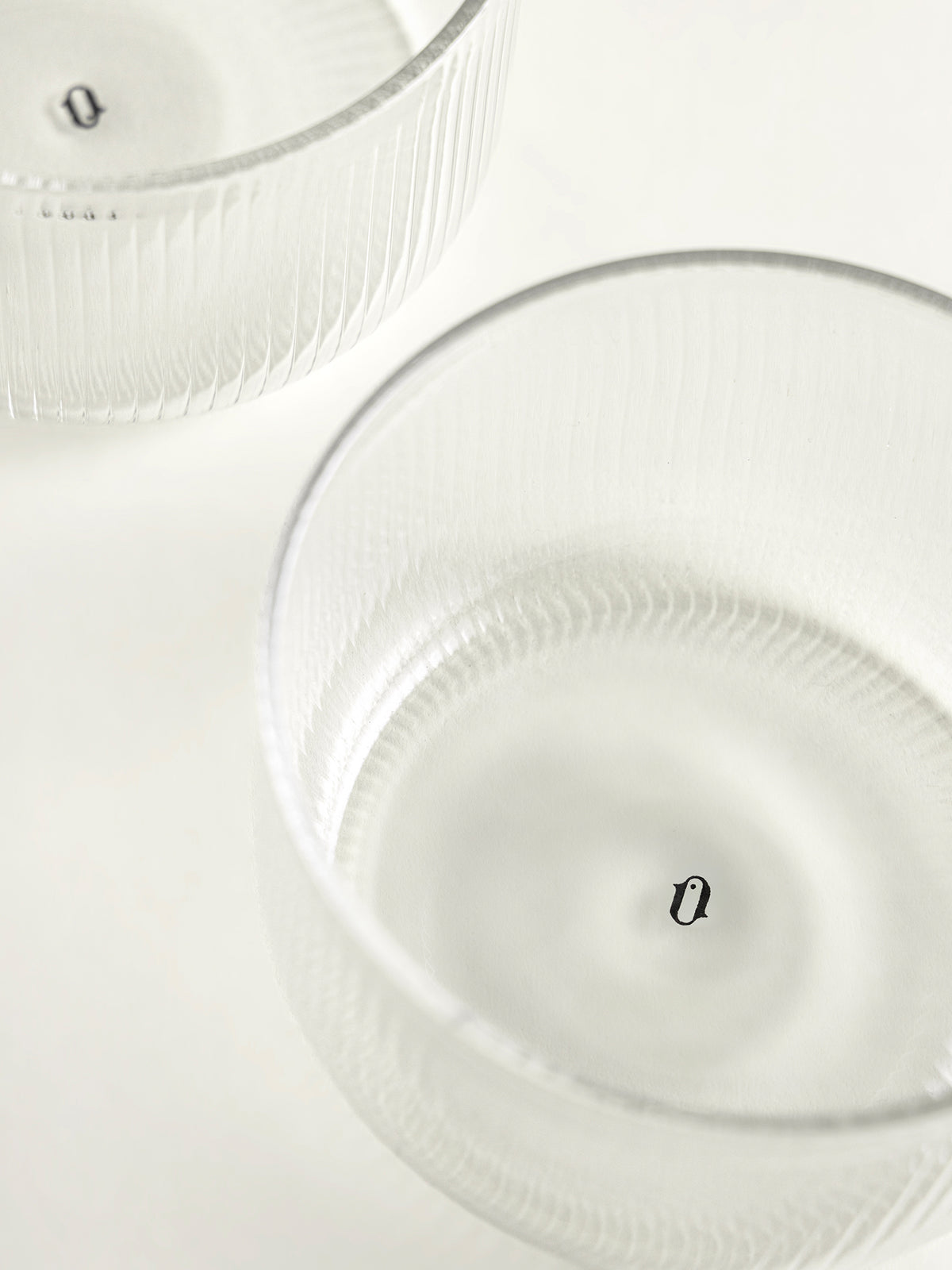 Two clear ribbed glass bowls on a white surface, photographed from above with soft lighting and logo printed inside each bowl.
