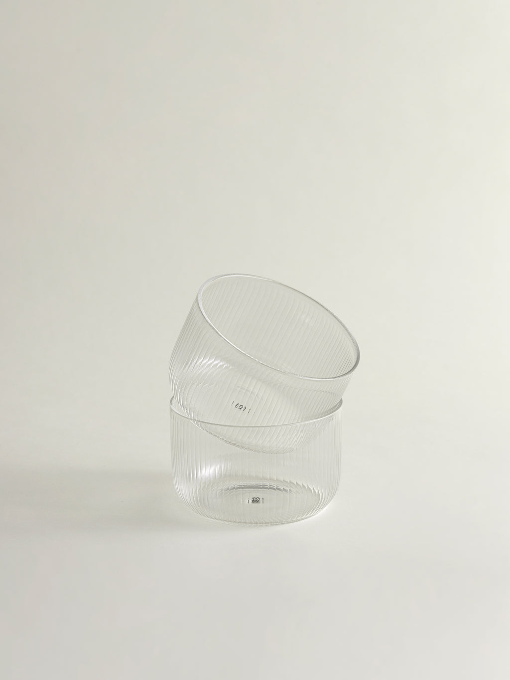 Two clear ribbed glass bowls stacked slightly offset on a plain off-white background.