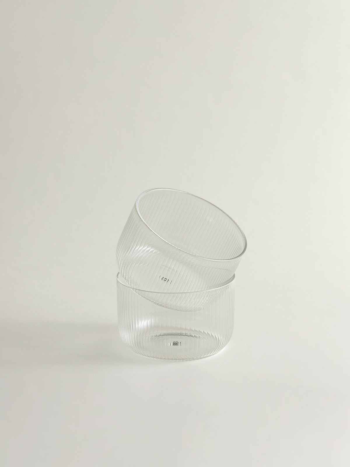 Two clear ribbed glass bowls stacked slightly offset on a plain off-white background.