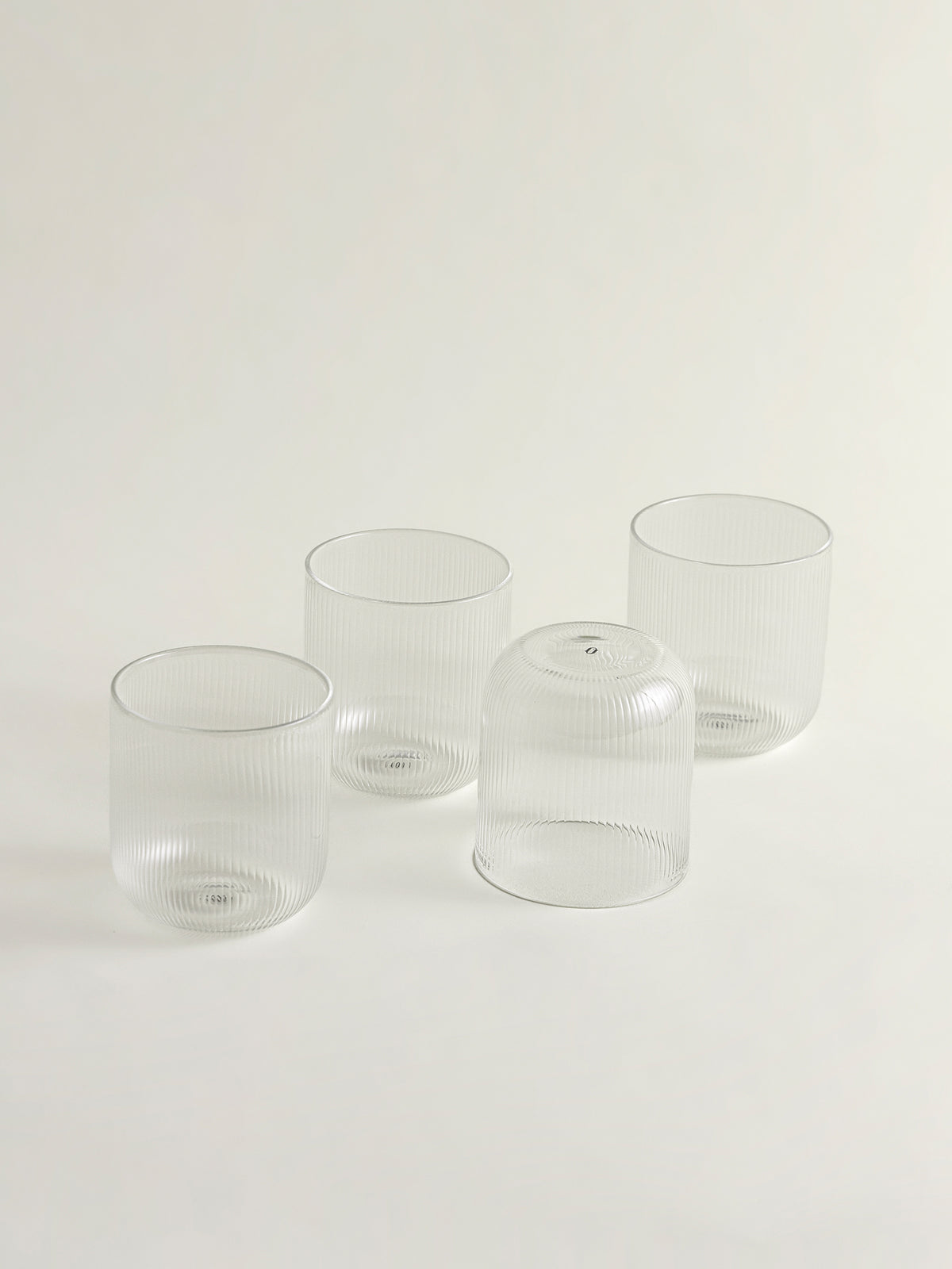 Four clear ribbed glass tumblers arranged on a plain white studio background.