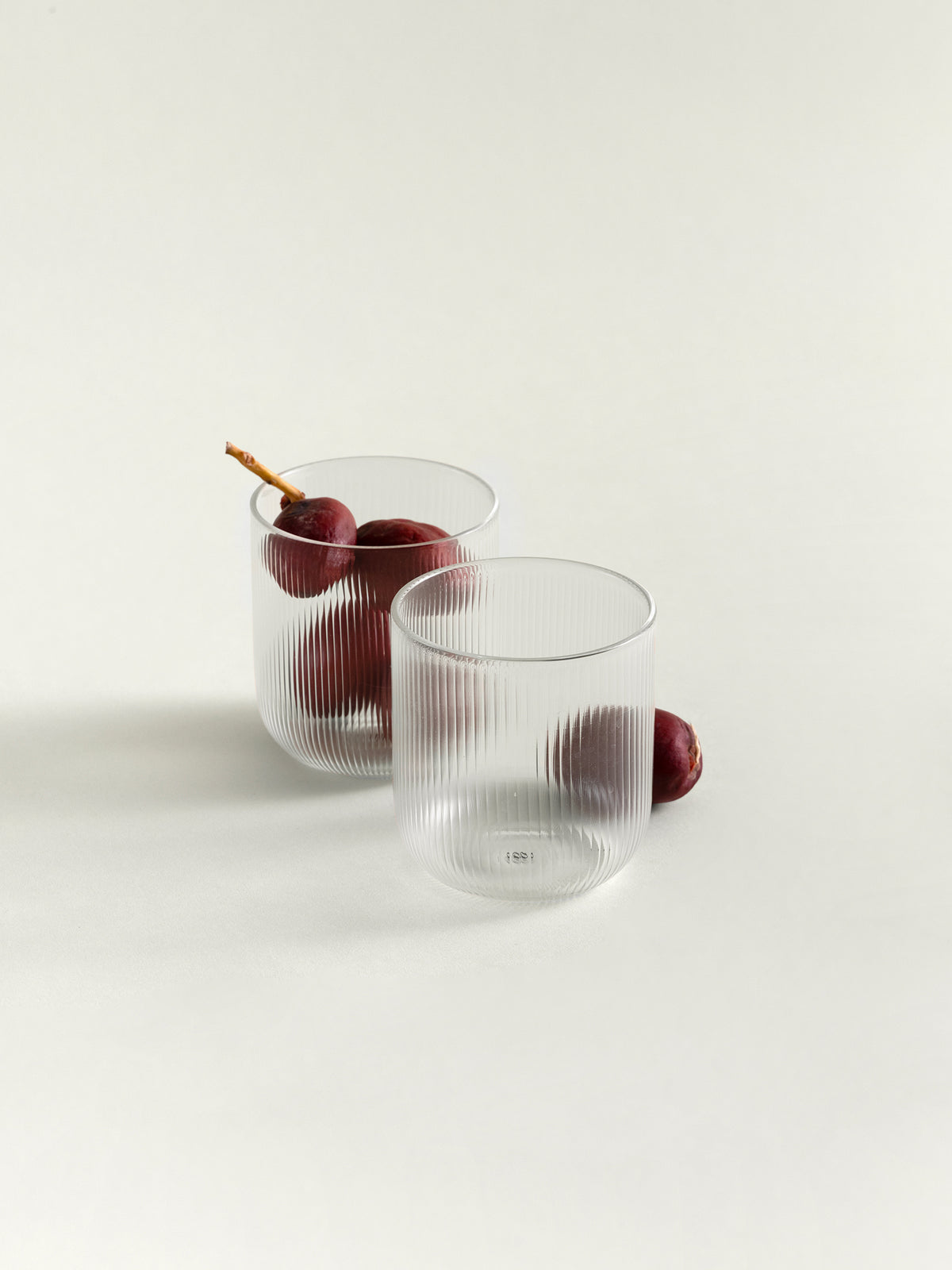 Two clear ribbed glass tumblers on a white studio background, with a few dark red dates placed inside and beside them.