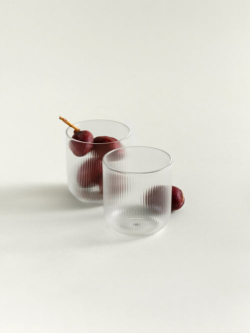 Two clear ribbed glass tumblers on a white studio background, with a few dark red dates placed inside and beside them.