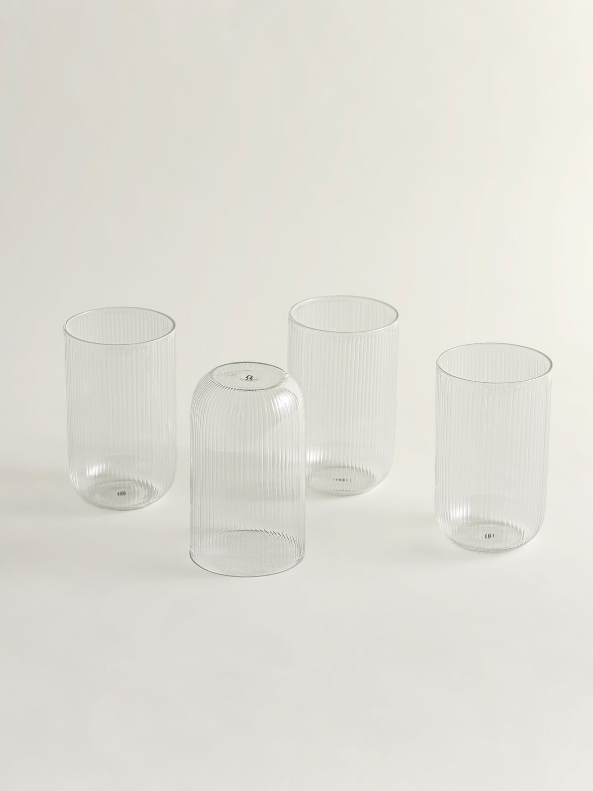 Four clear ribbed glass tumblers with a flared rim, arranged on a seamless light gray background.
