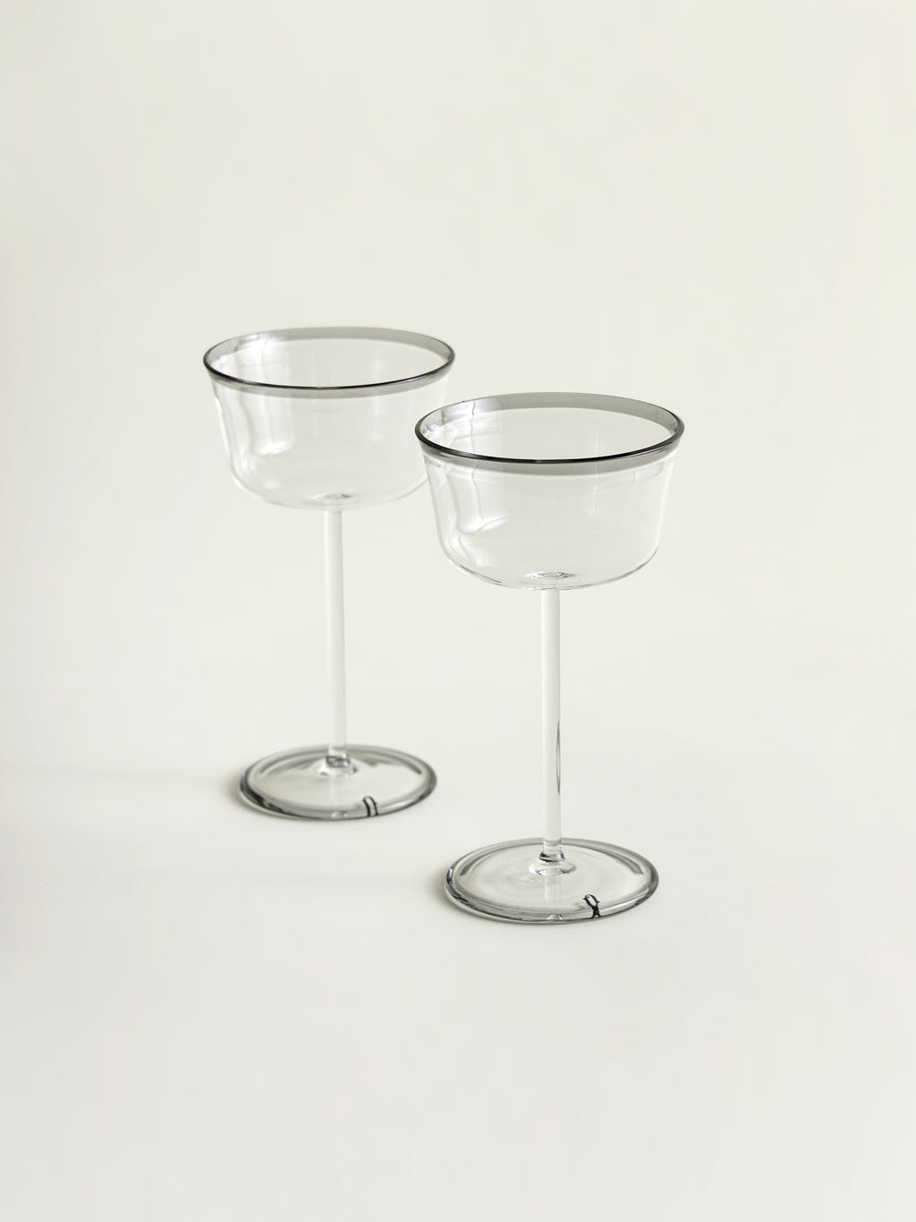Two clear stemmed coupes with thin smoke grey rims, standing on a light neutral background.