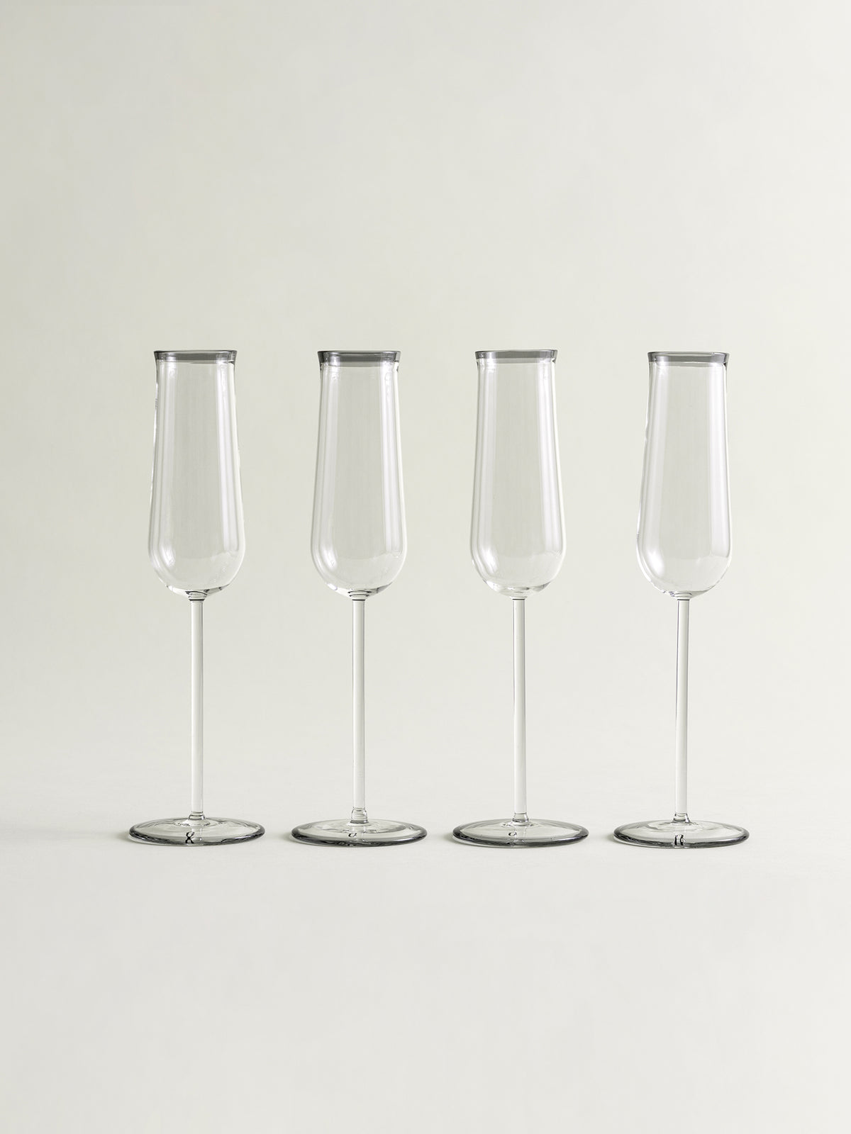 Four clear champagne flutes with smoke grey rims, arranged in a row on a light gray background.