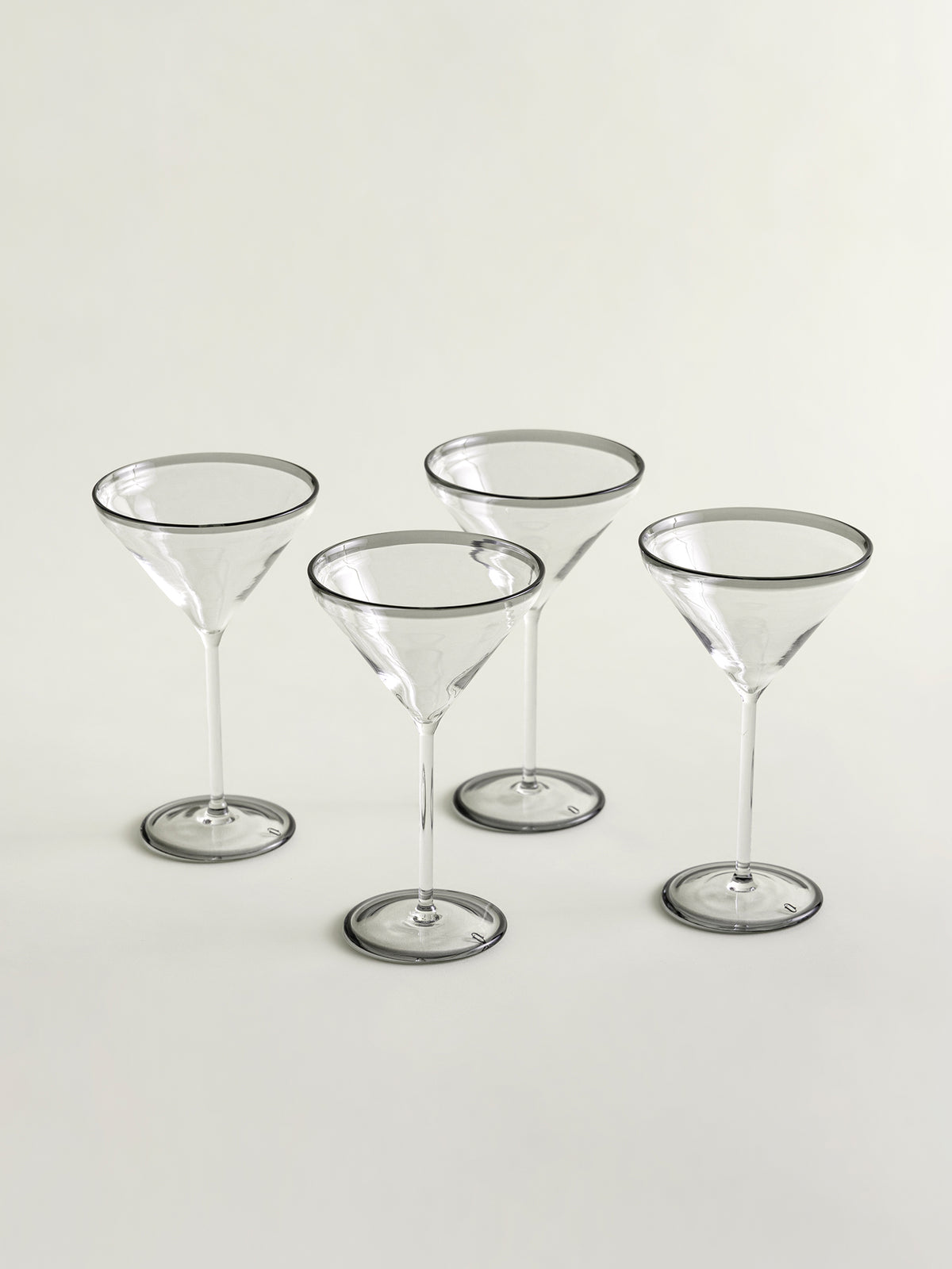 Four clear martini glasses with thin smoke grey rims, arranged on a plain light background.