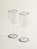 Two clear wine glasses with a smoke grey rim, standing on a light beige background.