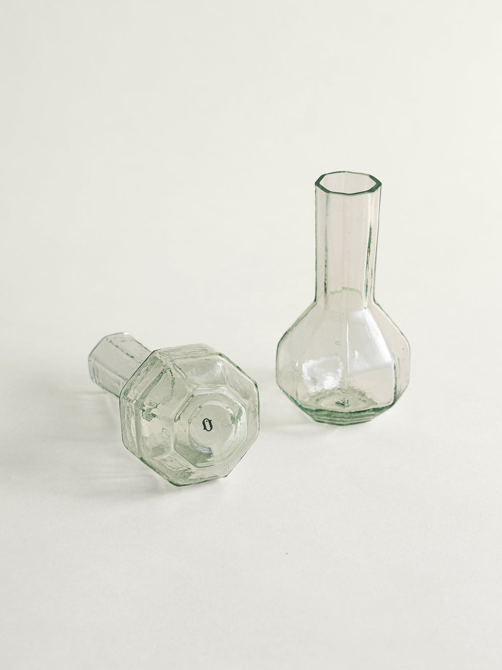 Two clear glass bud vases with faceted octagonal bases, one standing upright and the other lying on its side, photographed on a clean off-white background.