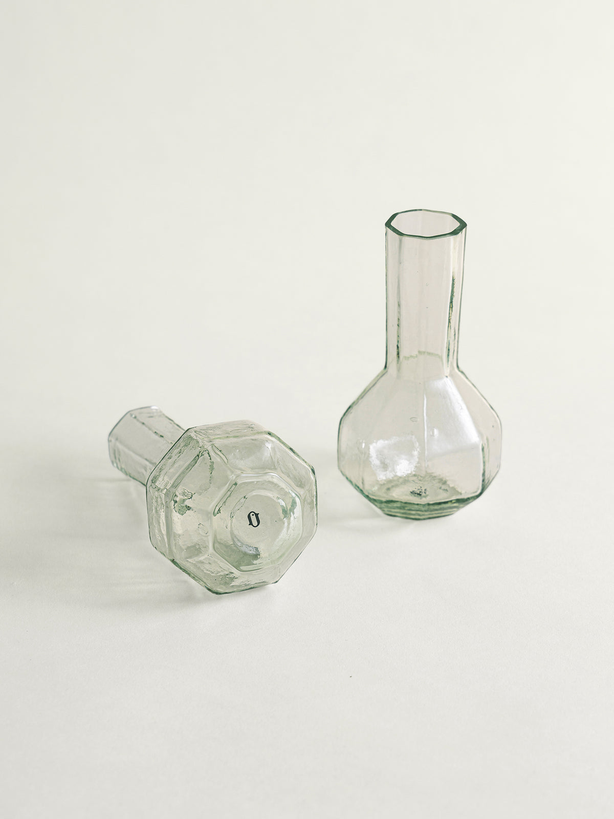 Two clear glass bud vases with faceted octagonal bases, one standing upright and the other lying on its side, photographed on a clean off-white background.