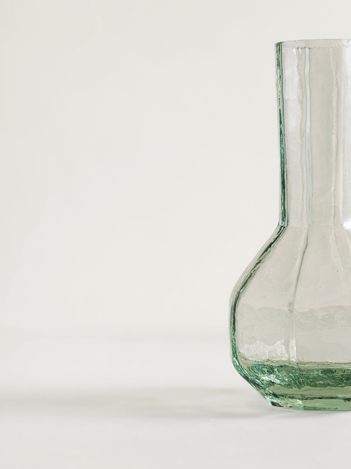 A clear textured glass vase with a bulbous base and a narrow neck, shown on a plain off-white background.