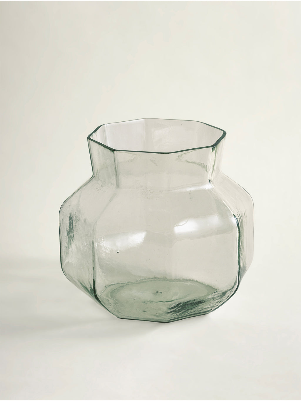 A clear glass vase with a wide, rounded body and a narrow neck, featuring a subtle green tint and a faceted geometric design, set against a plain light background.
