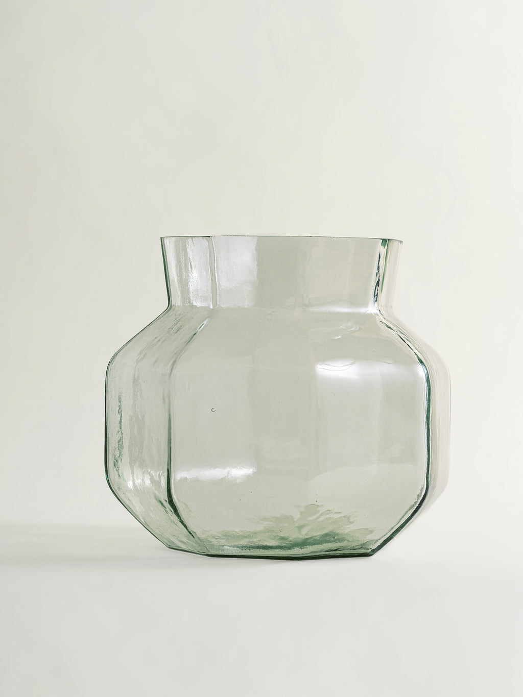 A clear glass vase with a rounded, multi-sided geometric body and a flared rim, shown on a plain light background.
