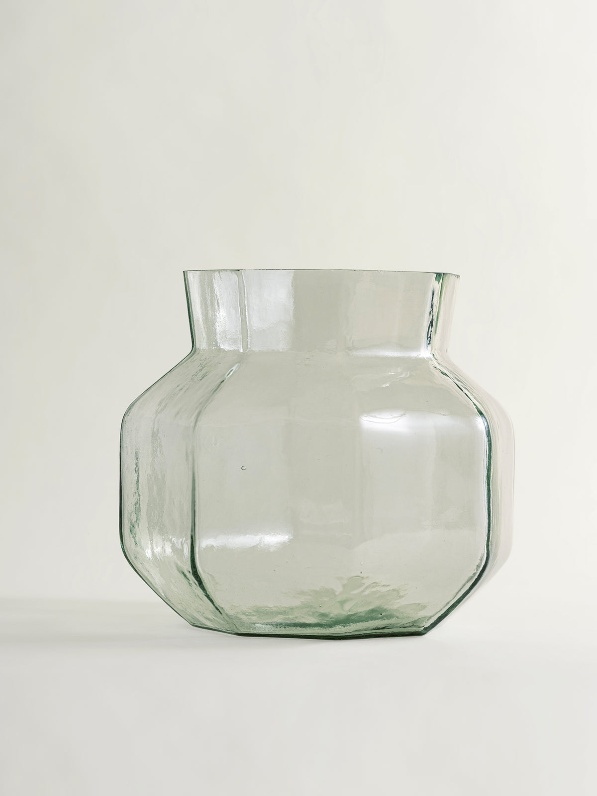 A clear glass vase with a rounded, multi-sided geometric body and a flared rim, shown on a plain light background.