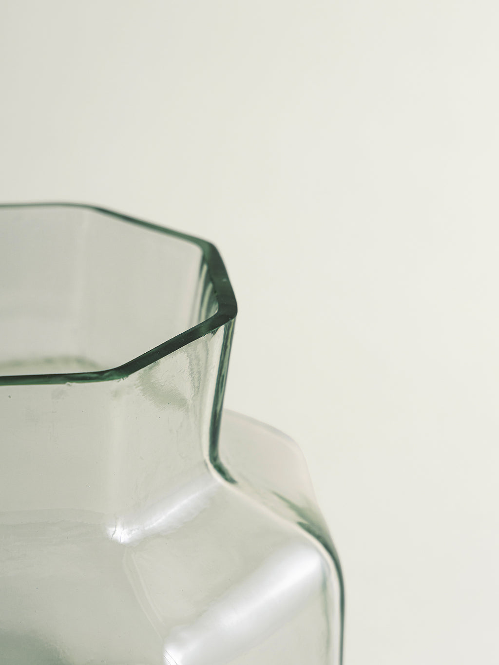 Close-up of a clear glass vase with a octagonal rim and a faceted, rounded body, photographed against a plain off-white background.