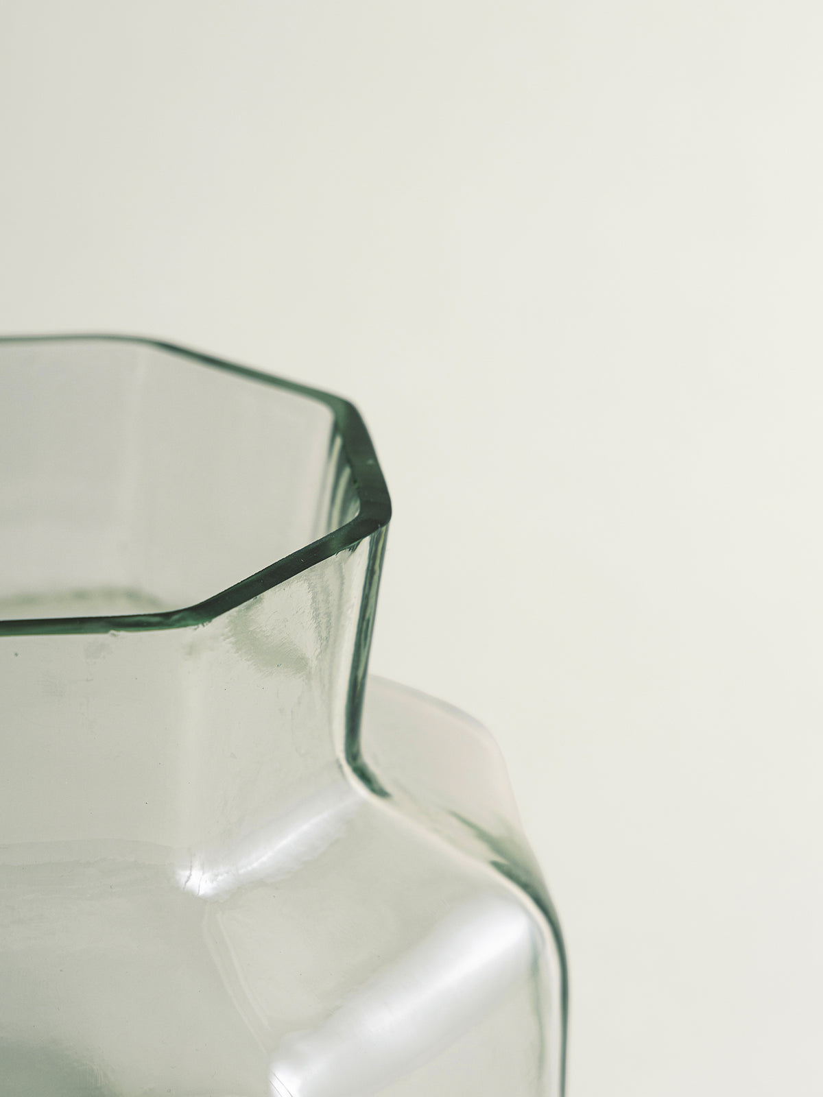 Close-up of a clear glass vase with a octagonal rim and a faceted, rounded body, photographed against a plain off-white background.