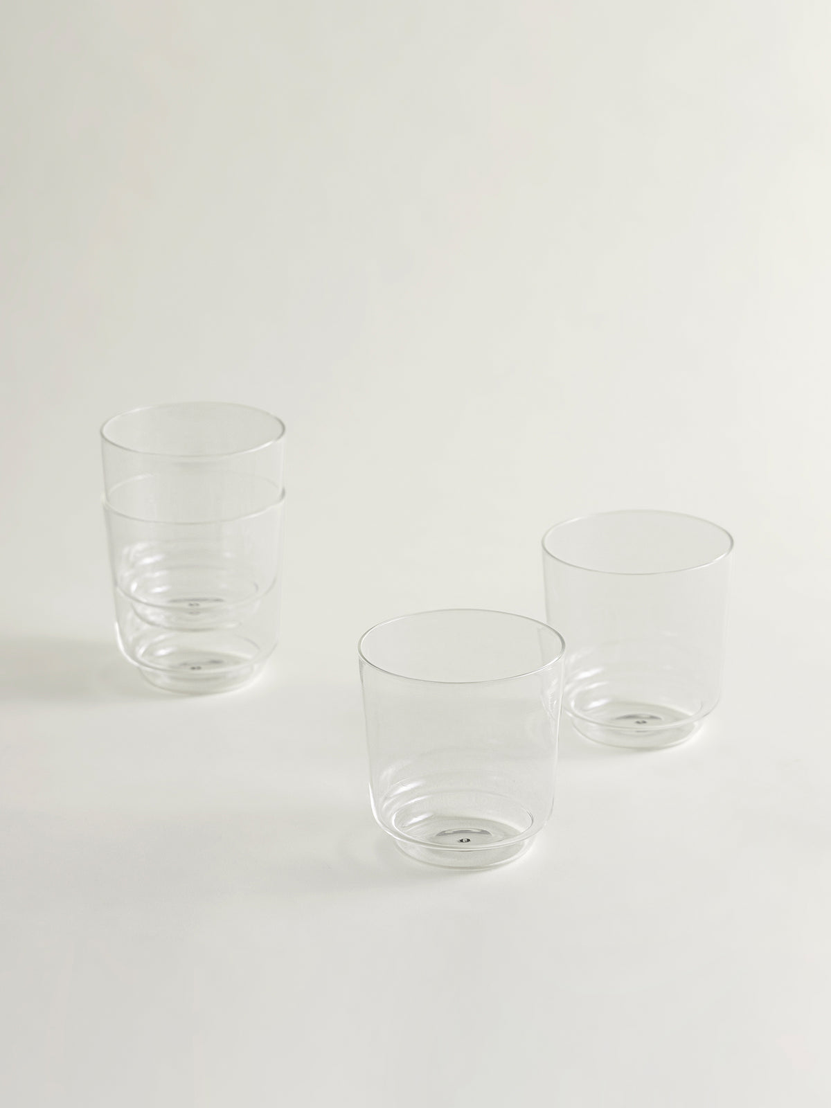 Four clear glass tumblers, stacked, arranged on a seamless light gray background.