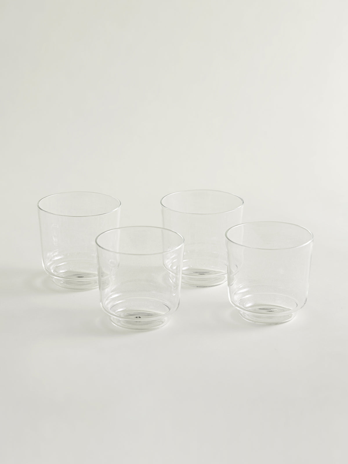 Four clear glass tumblers arranged in a loose square on a clean white studio background.