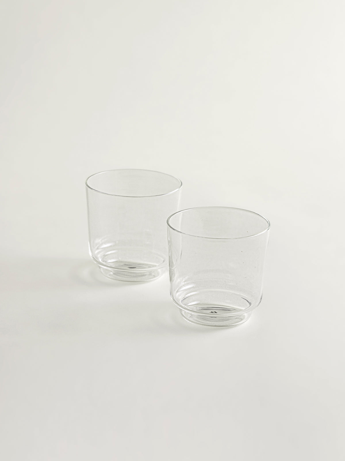 Two clear glass tumblers with a slightly tapered shape, standing on a plain white surface against a white background.