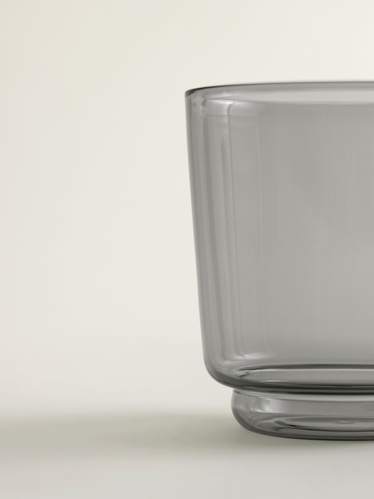 A close-up of a translucent smoke grey glass container on a light neutral background.