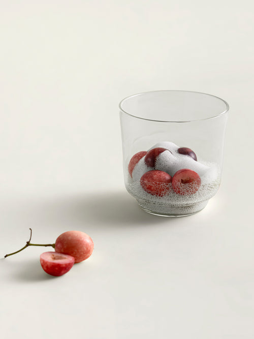 A clear glass containing red karondas and white foam, photographed on a clean off-white surface with a couple of loose karondas beside it.