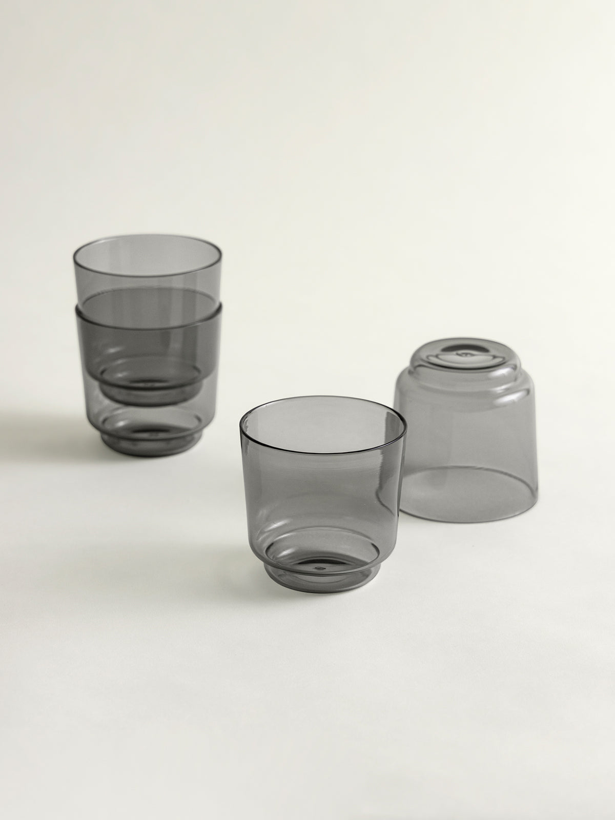 Four translucent smoke grey borosilicate glasses arranged on a clean white studio background.