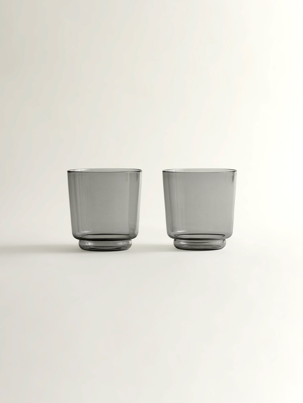 Two translucent smoke grey glass tumblers with a modern tapered shape, shown on a clean off-white background.