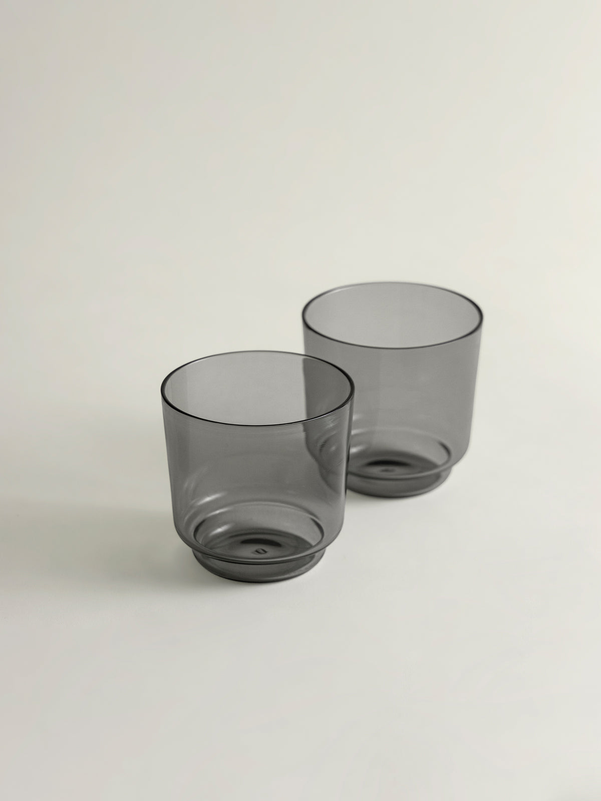 Two translucent smoke grey glass tumblers with a modern tapered shape, shown on a clean off-white background.