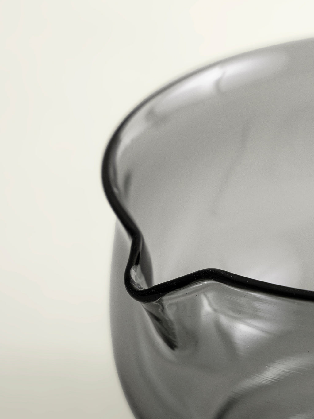 Close-up of a translucent smoke grey glass whisking bowl, photographed against a clean off-white background.