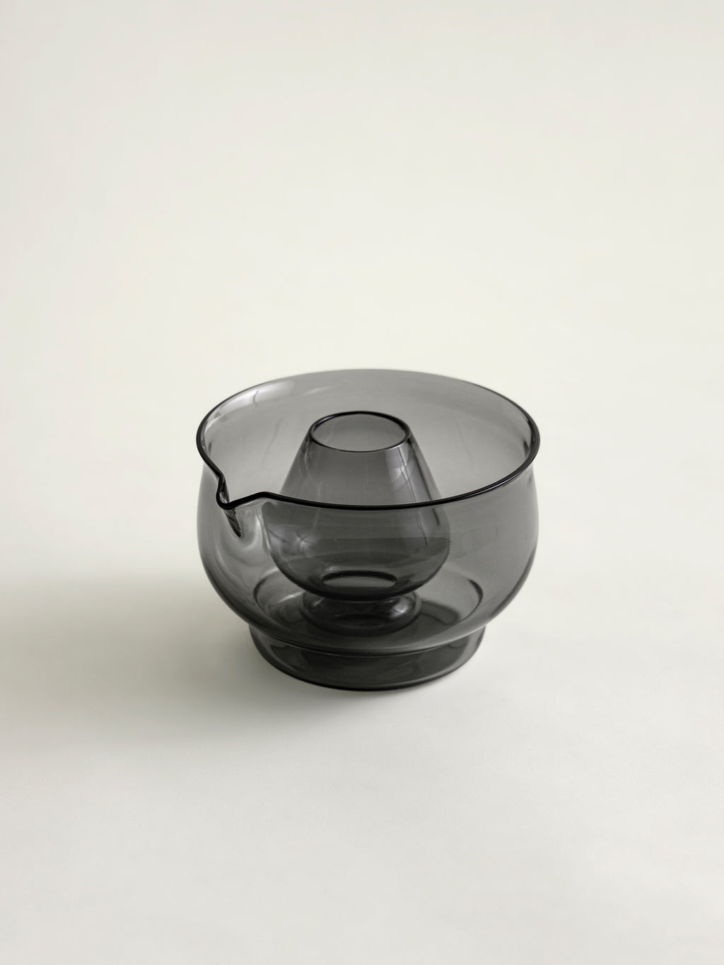 A smoke grey translucent glass bowl with a matcha whisk holder in the center, set against a plain light gray background.