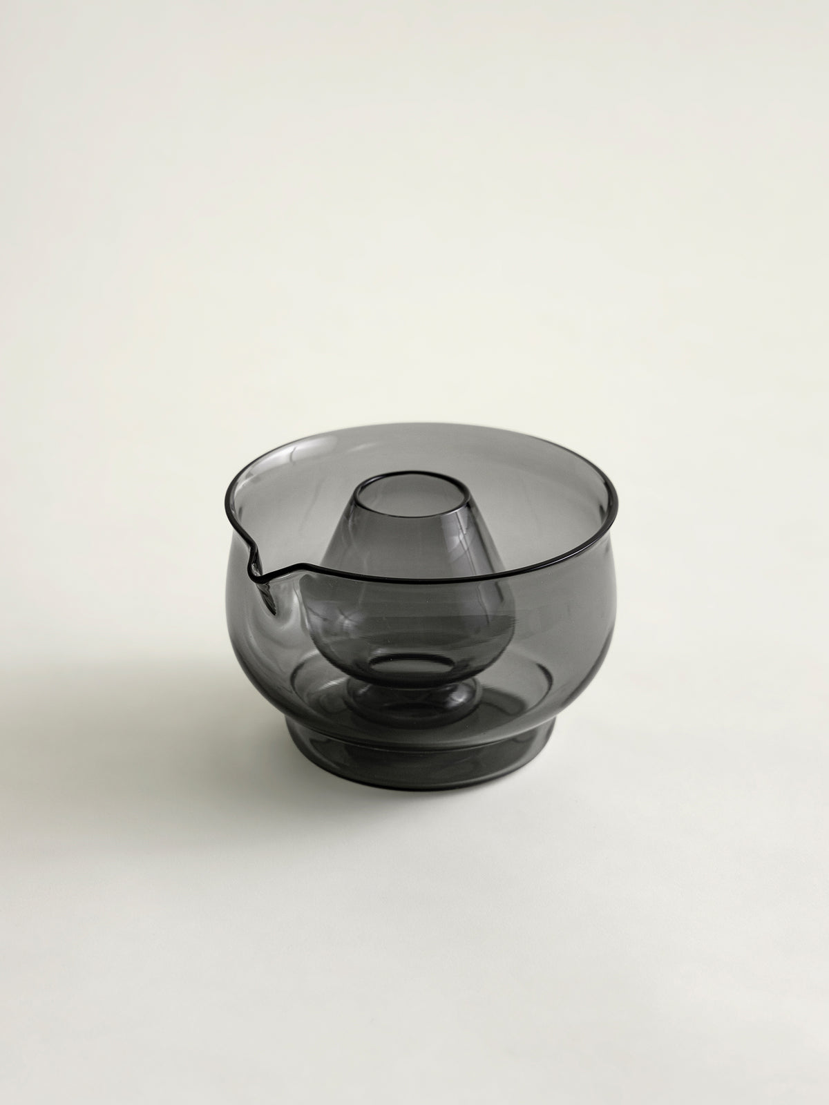 A smoke grey translucent glass bowl with a matcha whisk holder in the center, set against a plain light gray background.