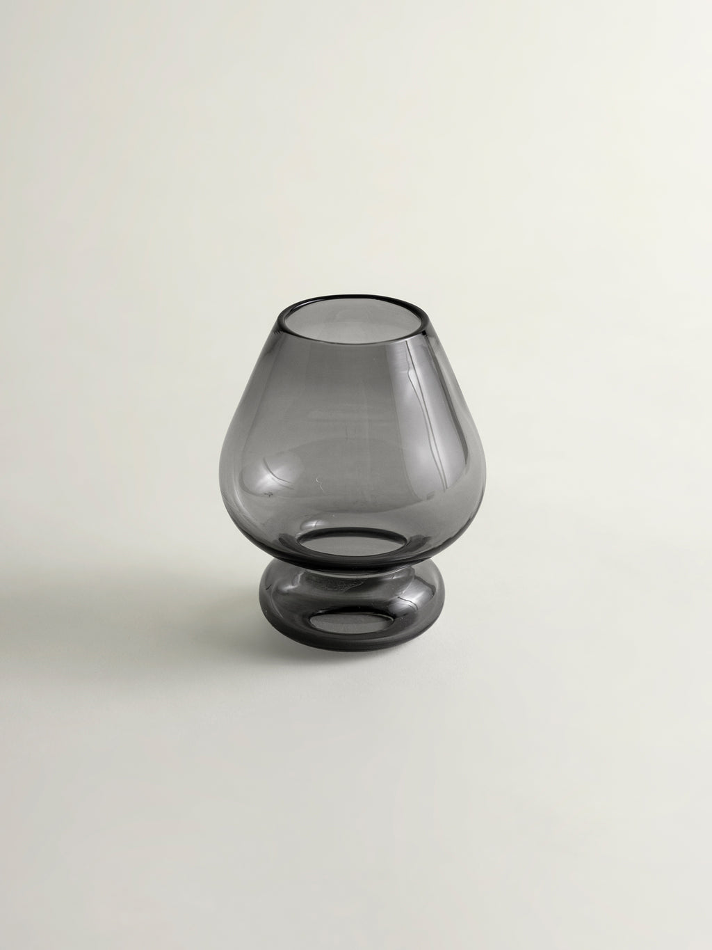 A translucent smokey grey matcha whisk holder with a flared rim and a short pedestal base, photographed against a plain light gray background.