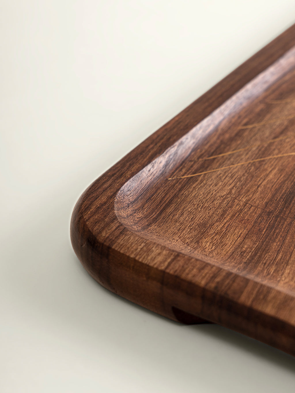 Close-up of a dark brown wooden serving tray corner with rounded edges and visible wood grain on a light neutral background.