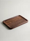 A rectangular dark brown wooden tray with rounded corners and a carved wave-like pattern in the center with brass threads, shown on a light gray background.