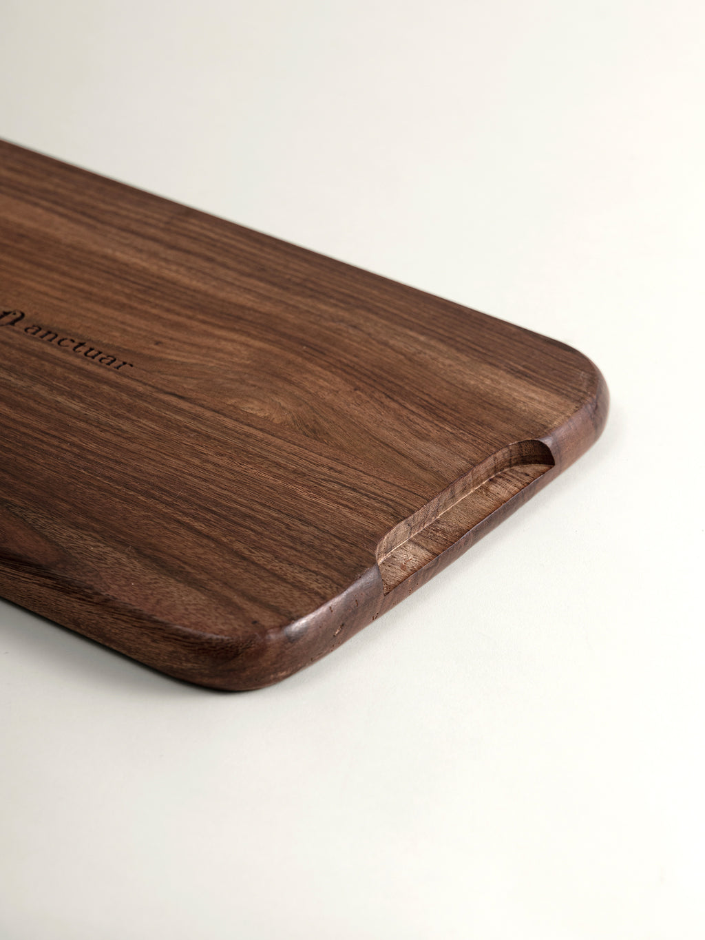 A close-up of a dark brown rosewood tray with rounded corners and a cutout handle, featuring the engraved brand name 'anctuar' on a clean white background.