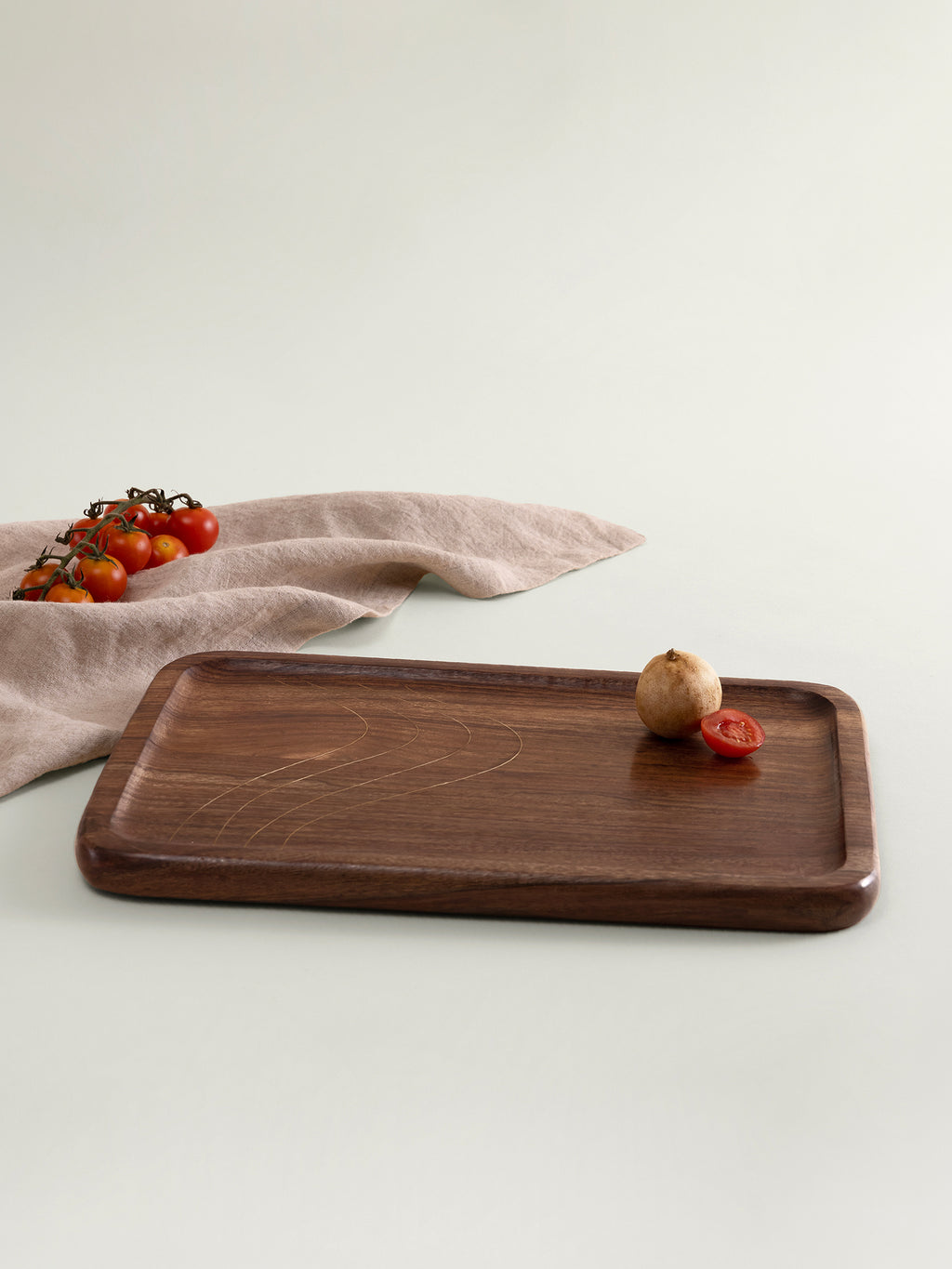 A rectangular dark brown wooden serving tray with rounded corners, styled on a light beige surface with a beige cloth and small food props.