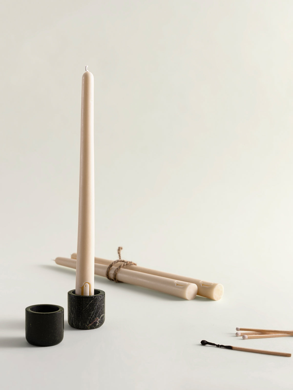 A marble candle holder set featuring a tall beige taper candle standing upright in the textured holder, with several matching candles wrapped in twine on a clean off-white background.