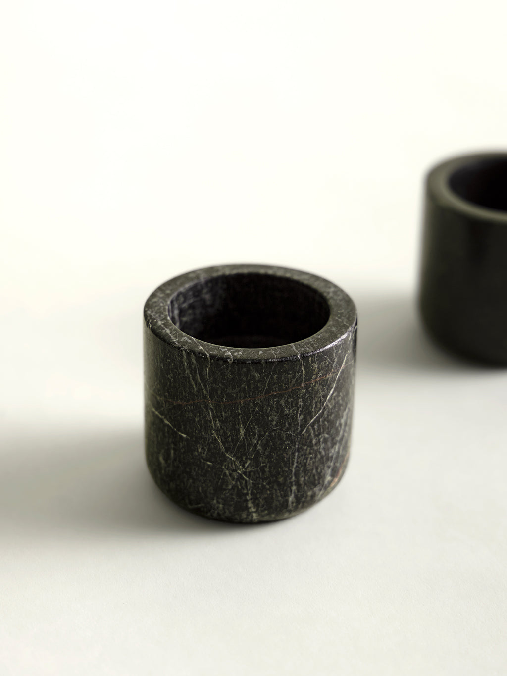 A close-up of a small rainforest marble candle holder with visible natural fissures, photographed on a clean white surface with another similar candle holder  partially visible in the background.
