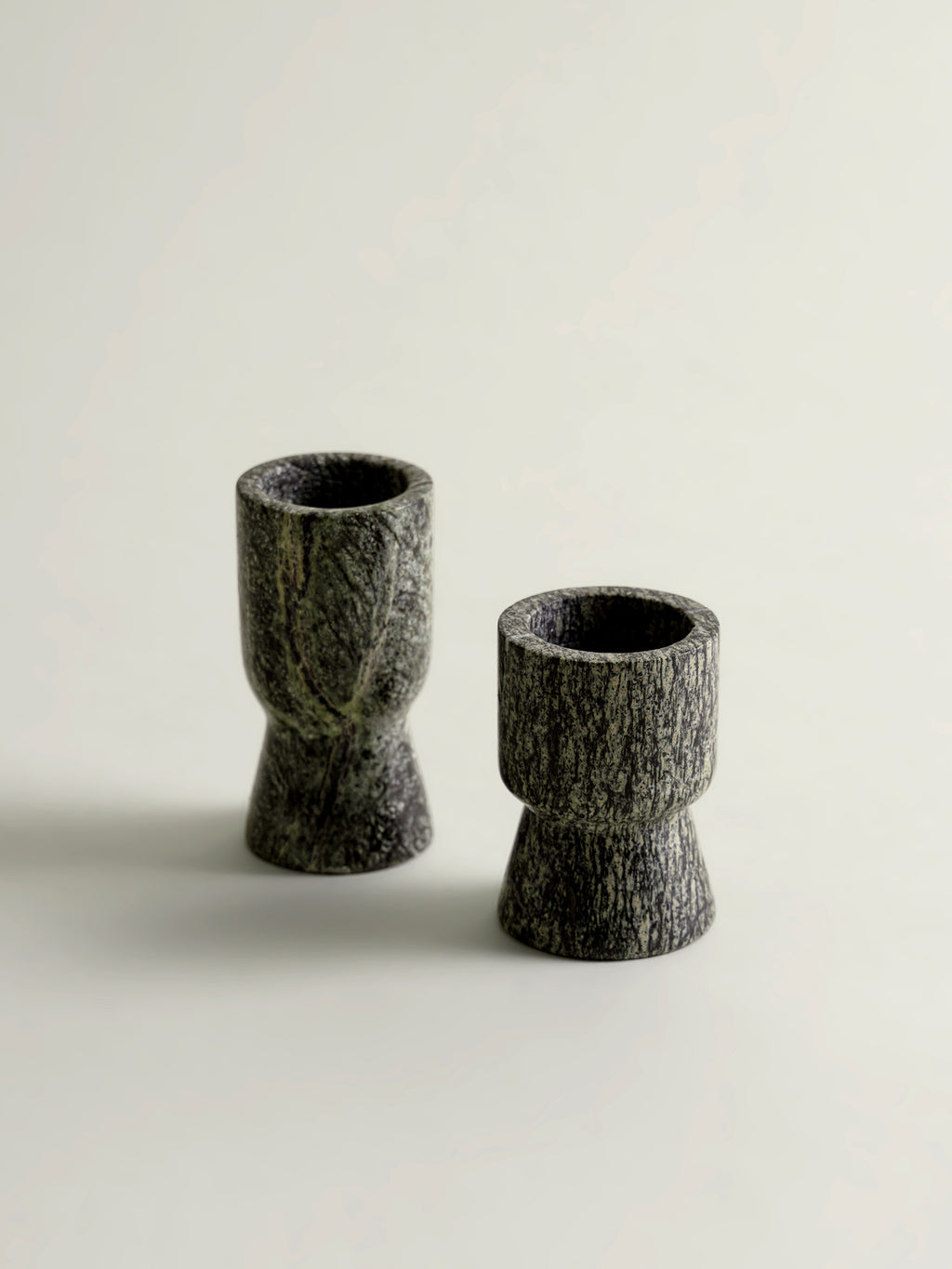 Two small rainforest green stone candle holders with a textured, bark-like finish, standing on a light beige surface against a neutral background.