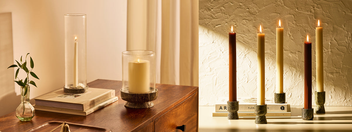 A set with multiple candle holders and lanterns in different shapes and sizes with ribbed and plain candles, displayed on a wooden table alongside books.
