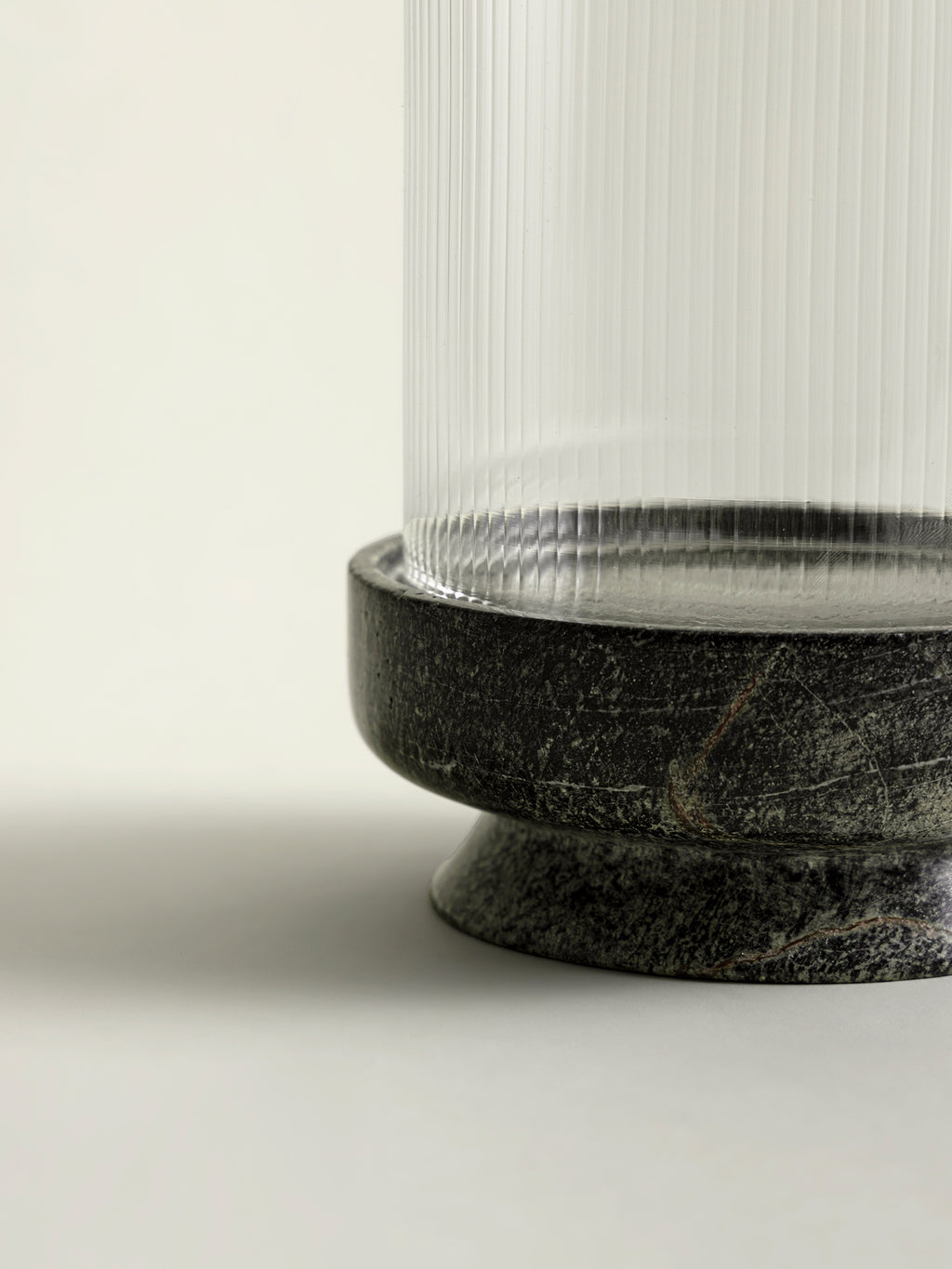Close-up of a lantern base featuring a round, green speckled marble base and a clear ribbed glass shade.