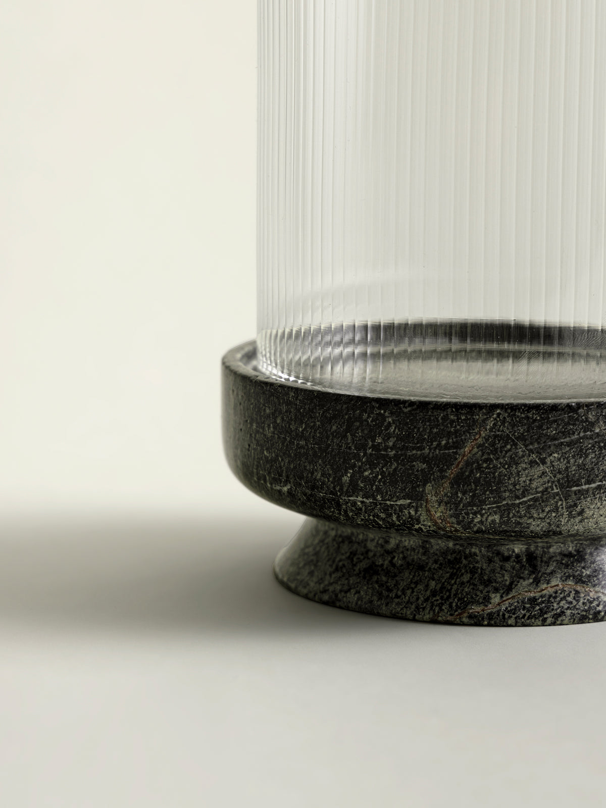 Close-up of a lantern base featuring a round, green speckled marble base and a clear ribbed glass shade.