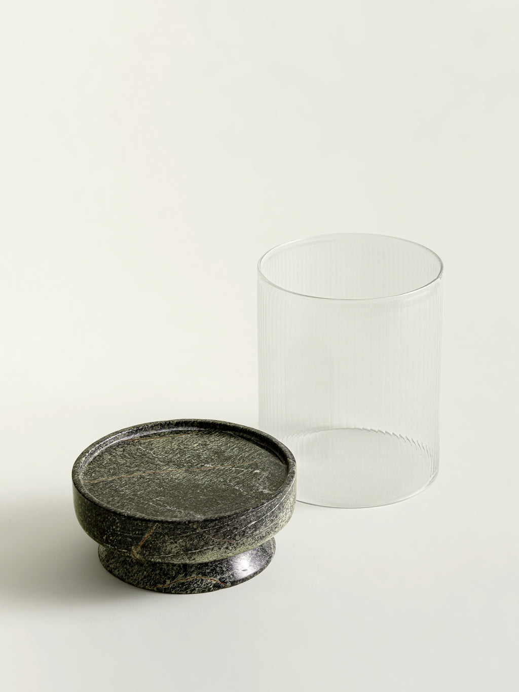 A green textured marble lantern base positioned next to a ribbed clear glass cylinder on a clean off-white background.