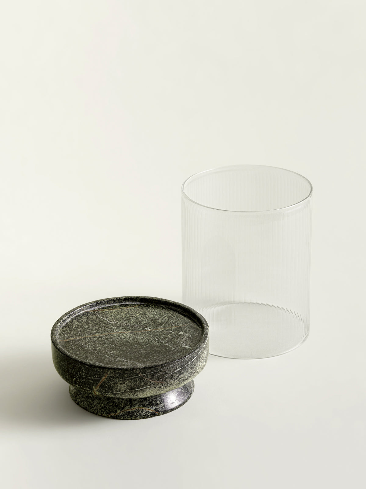 A green textured marble lantern base positioned next to a ribbed clear glass cylinder on a clean off-white background.