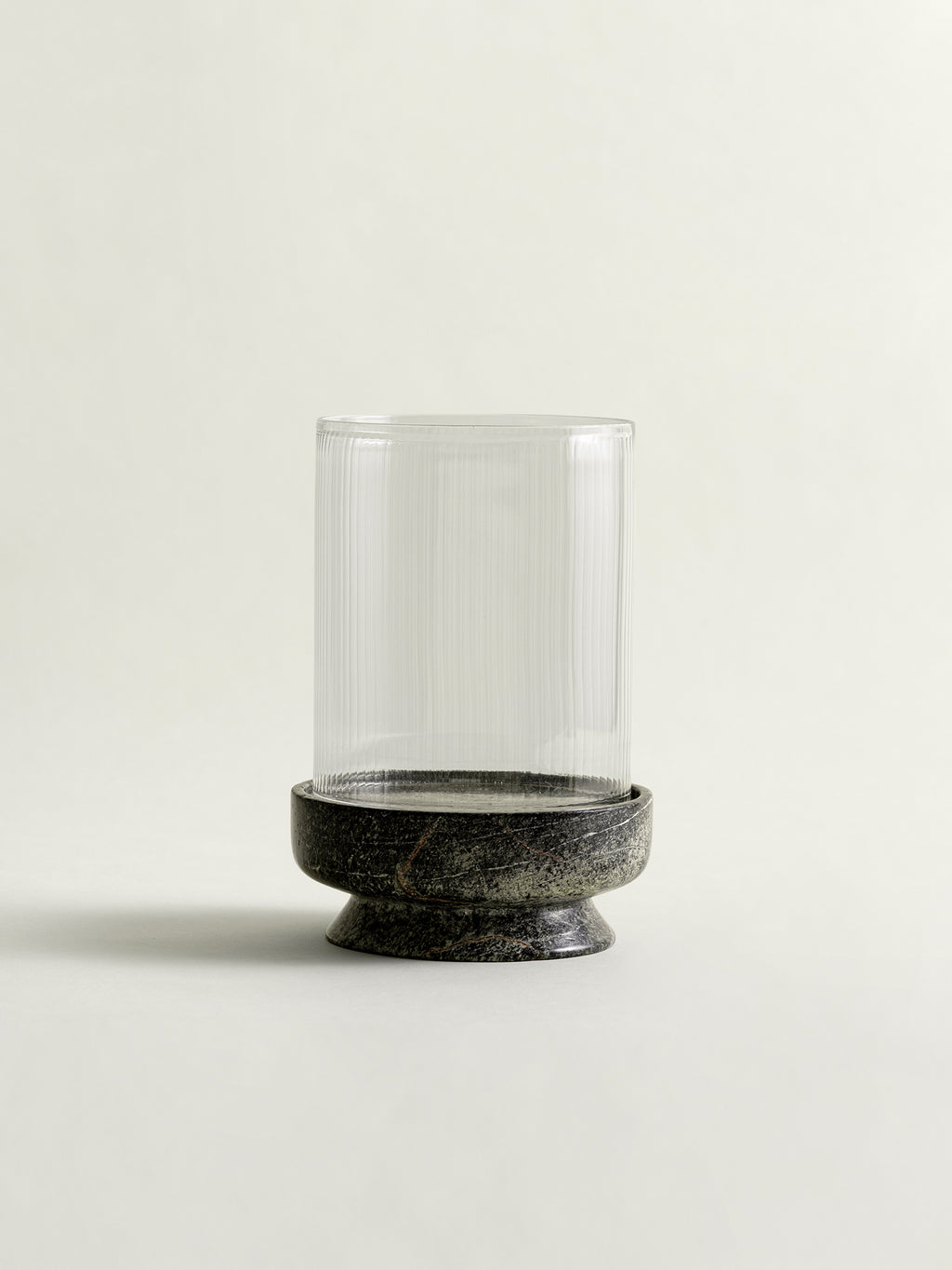 A clear ribbed glass cylinder candle holder with a rainforest green marble base, photographed against a plain light beige background.