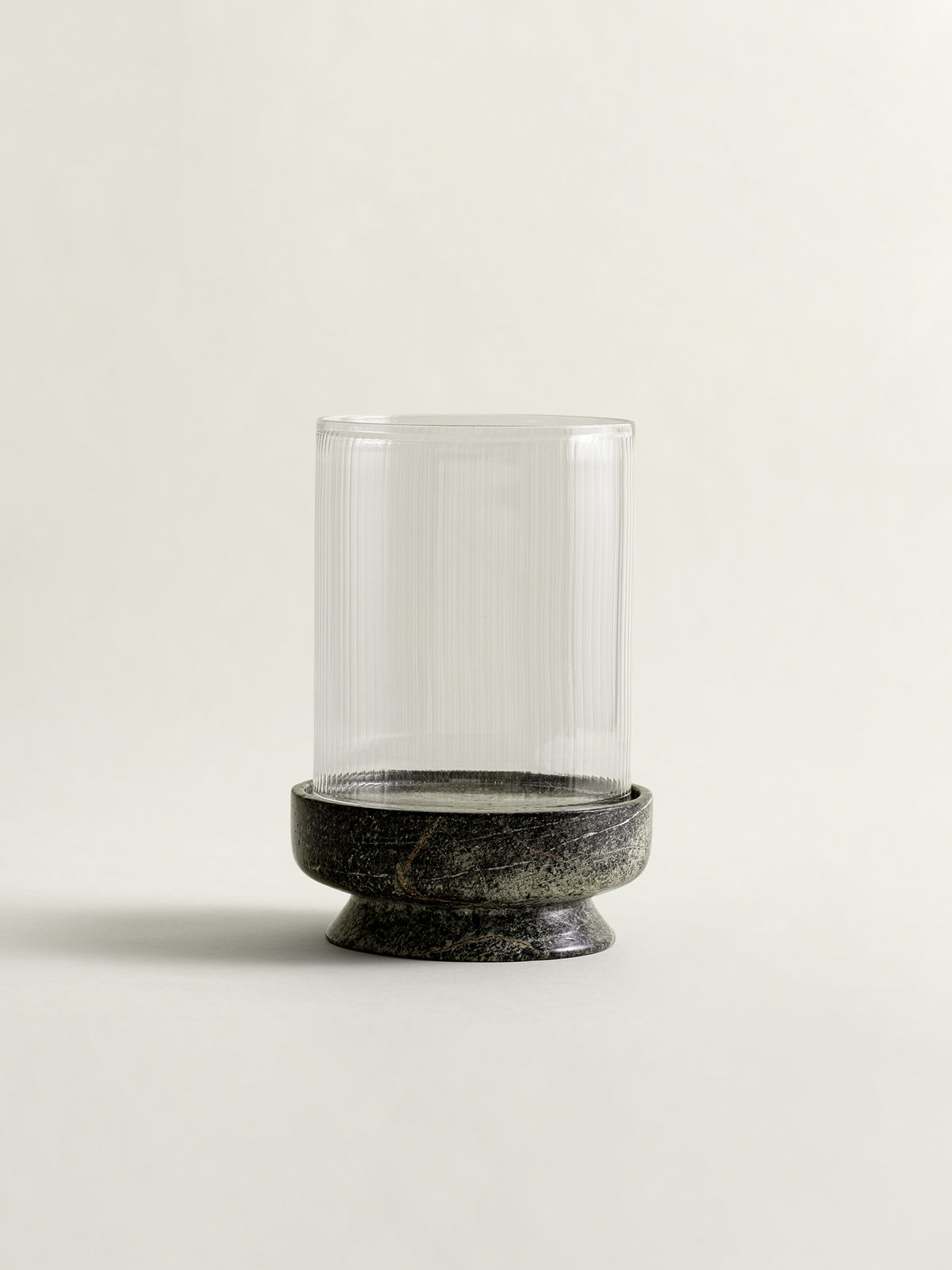 A clear ribbed glass cylinder candle holder with a rainforest green marble base, photographed against a plain light beige background.