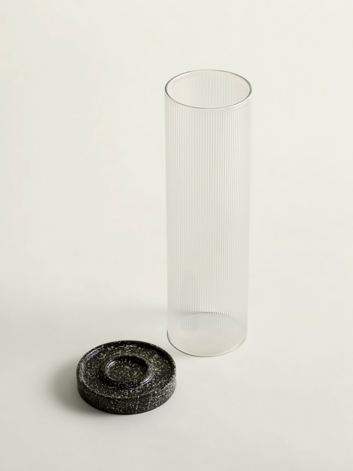 A tall, clear ribbed glass cylinder lantern top standing next to a small round green textured marble base on a clean off-white background.